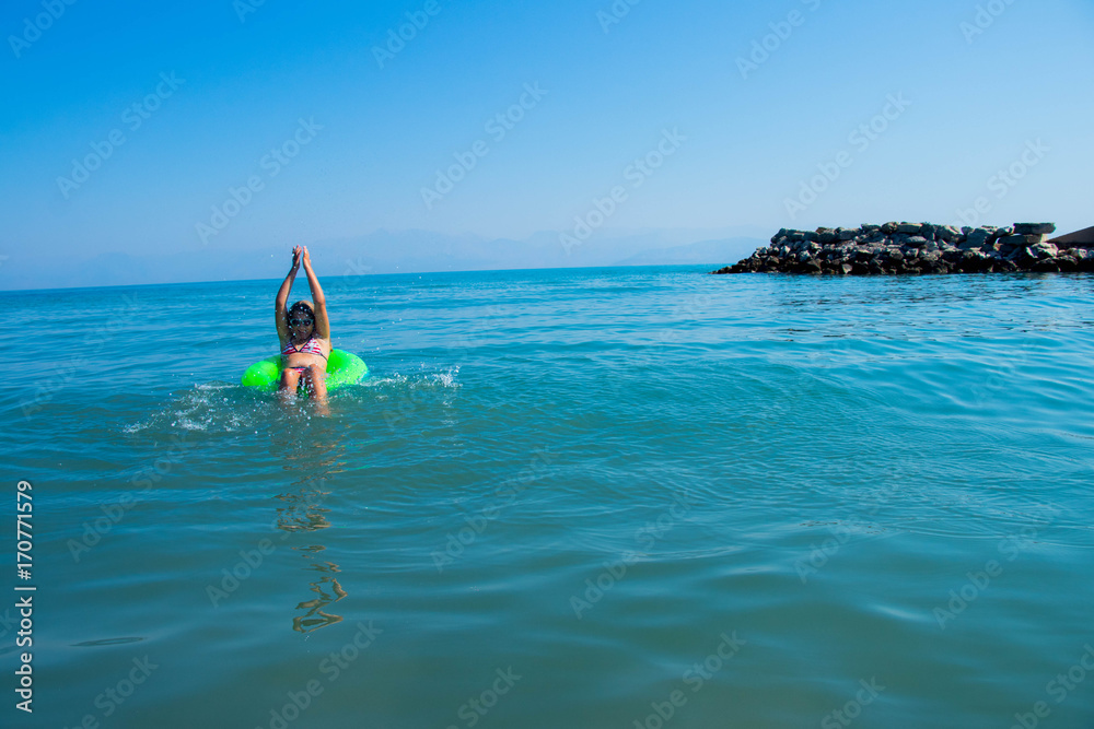 girl splashing water on a celadon wheel to swim in a turquoise sea against a blue sky on a beautiful summer day
