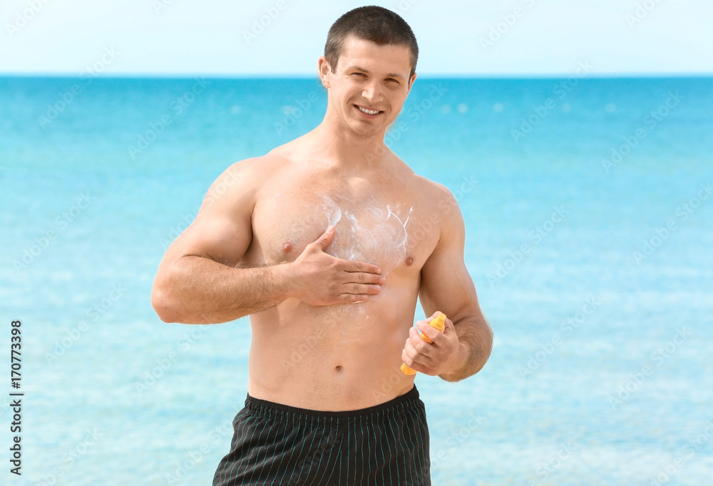 Handsome young man applying sunscreen cream on sea beach Handsome young man applying sunscreen cream on sea beach