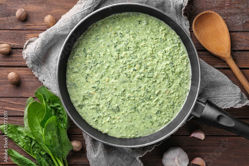 Frying pan with tasty spinach sauce on table