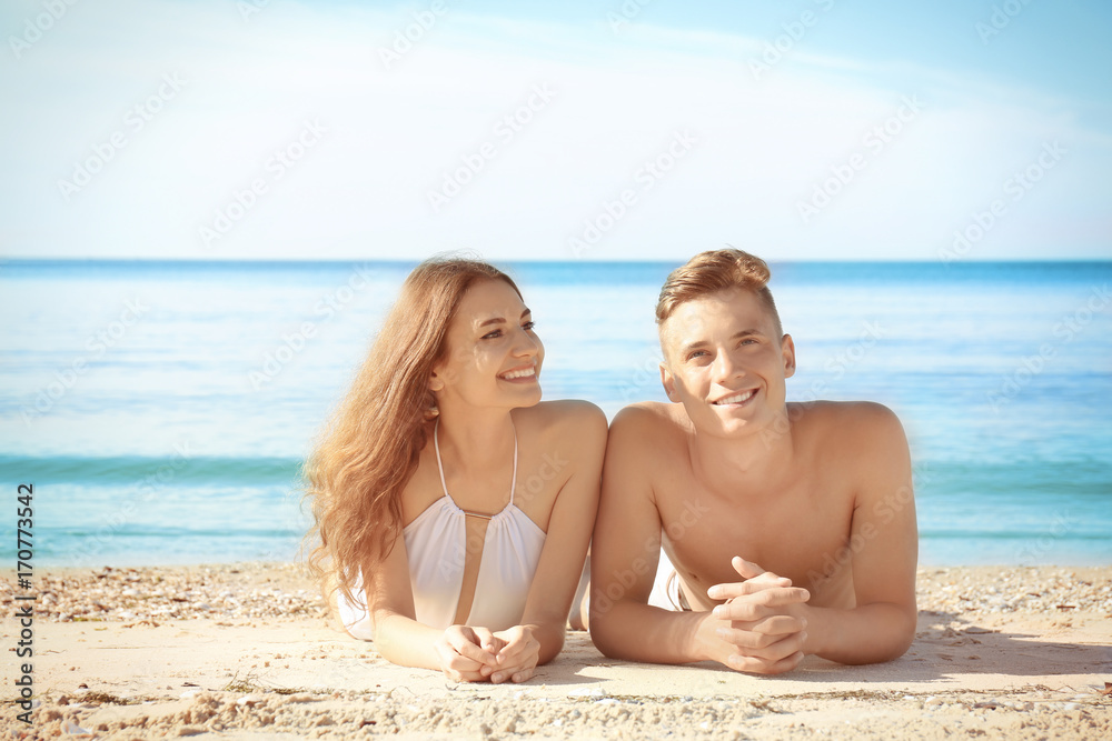 Happy young couple lying on sea beach at resort