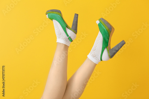 Female legs in green high heel shoes and socks on color background