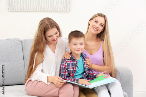 Lesbian couple reading with foster son at home. Adoption concept
