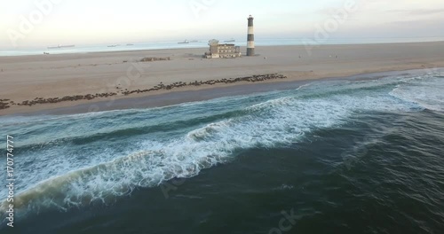 Aerial view footage of desert sand peninsula, old lighthouse and power station building on ocean seals beach, Walvis Bay lagoon view with sea background and ships at Namibia's Atlantic west coast photo