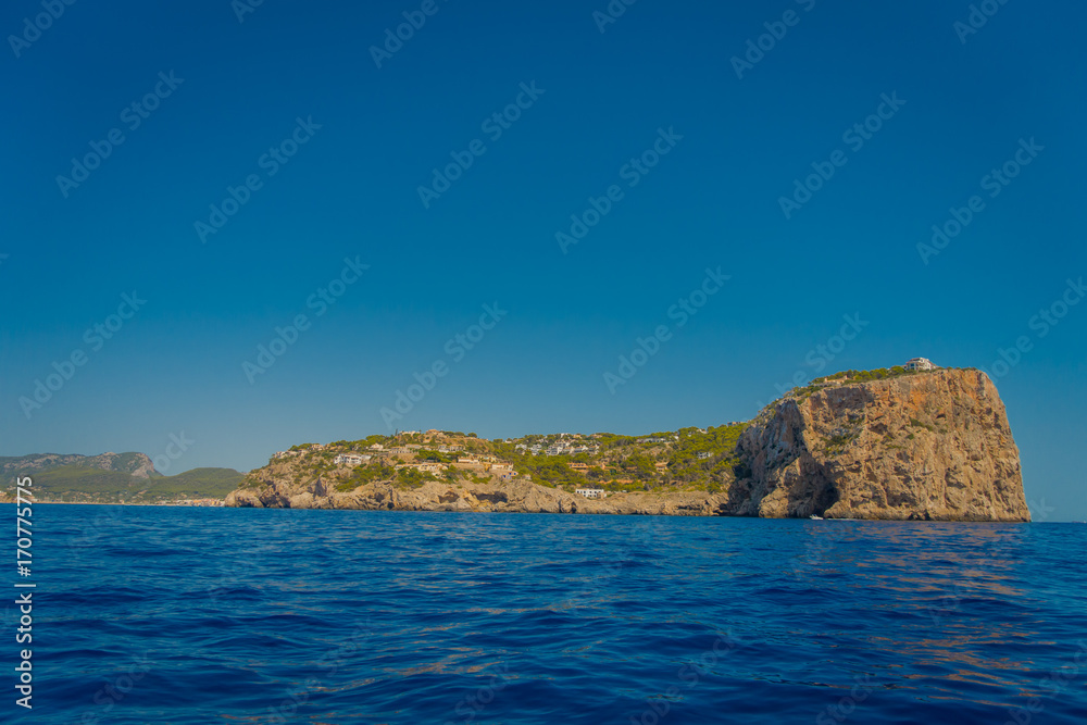 Beautiful view of Mallorca balearic islands, with some buildings in the mountain in the horizon, with gorgeous blue water and a beautiful blue sky, in Spain