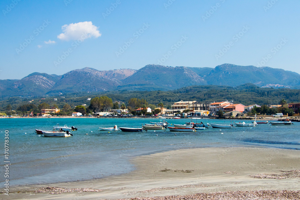 few  boats  on a calm blue sea with forested mountains in the background on a bright sunny day