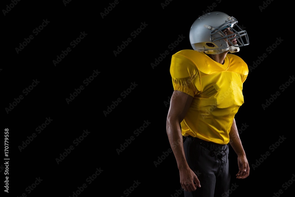 American football player standing against a black background