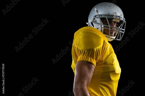 American football player standing against a black background