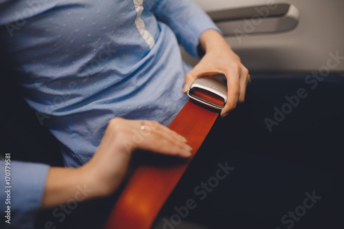 Girl passenger fastening seat while belt sitting on airplane