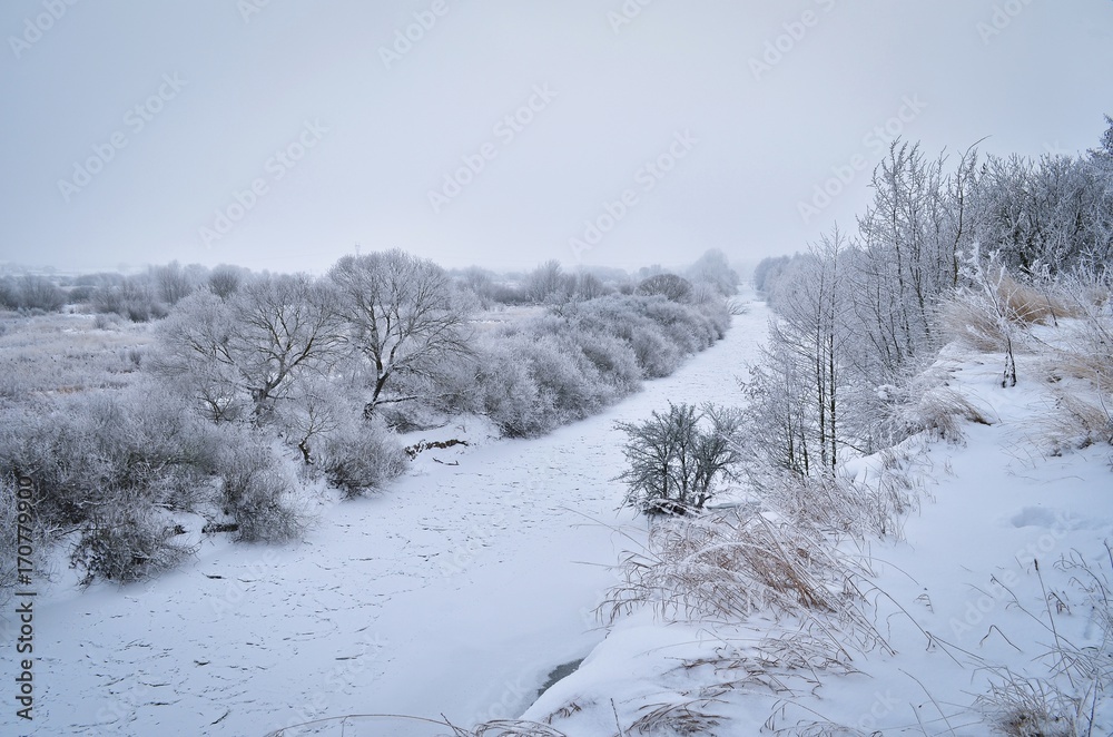 Beautiful winter scenery with frozen river and forest. Frosty winter atmosphere. Toned image. Beautiful winter scenery with frozen river and forest. Frosty winter atmosphere. Toned image.