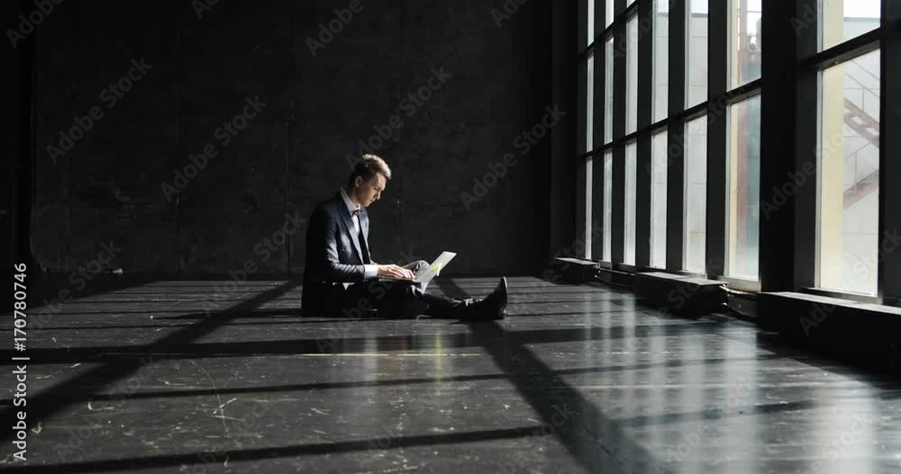 Successful young Man Working In Home Office in loft style. Stylish hipster man in a suit working against a blavk wall background lit by sunlight Successful young Man Working In Home Office in loft style. Stylish hipster man in a suit working against a blavk wall background lit by sunlight