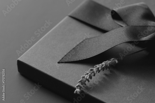 Black gift box on a dark contrasted background, decorated with a textured bow and feathers, creating a romantic atmosphere. Typically used for birthday, anniversary presents, gift cards, post cards, l