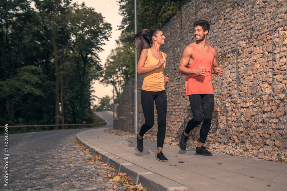 two young adult people, jogging, outdoors nature forest asphalt, sport clothes, happy smiling, looking at each other