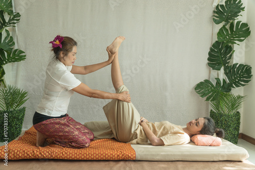Concept thai Massage. Beautiful Asian young woman getting thai herbal massage in spa salon.Thai girl stretching her legs with masseur.