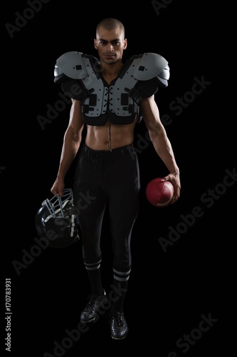 Muscular American football player holding football and head gear