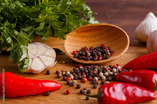 Fototapeta Naklejka Na Ścianę i Meble -  Spices in wooden spoon, close up. Mixed peppers on kitchen table, chilli peppers and parsley, ingredients for cooking.