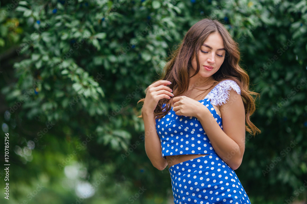 Fashion portrait of young pretty trendy girl with beautiful curly hair posing outdoors on background of green leaves