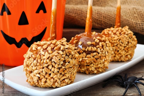 Halloween caramel apples with nuts on a plate with Jack o Lantern candy pail in background