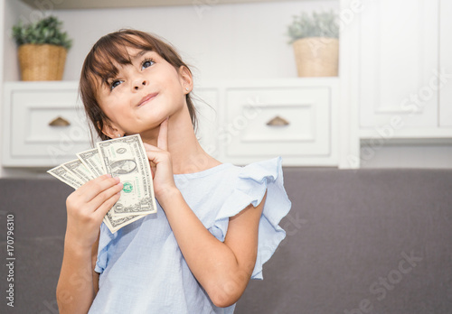 Cute little girl holding money in the living room, pretty girl thinking about how to spend her saving