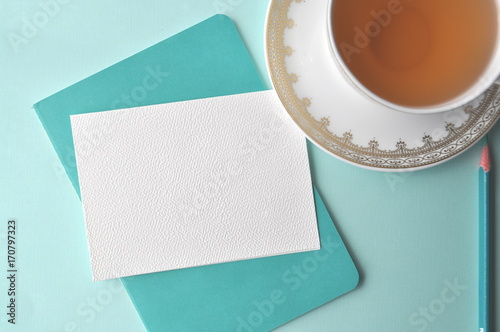 White fine china cup of tea with a blank note card and teal book on mint background