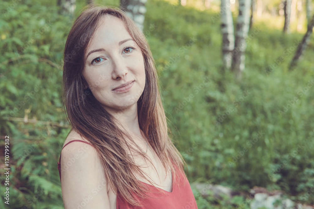 Young woman portrait in a summer forest in the mountains. Pretty girl in red dress in summertime