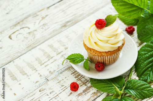 Delicate vanilla cupcakes with cream and raspberries on a white wooden background