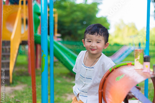 Young Asian boy play a iron train swinging at the playground under the sunlight in summer.