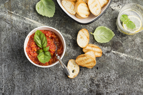 Healthy snack or lunch. Homemade tomato vegetable sauce with garlic, herbs, salt, butter, spices, fresh basil in a ceramic bowl with grilled toasts on a gray stone background. Top View. photo