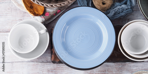 Ceramic and enamel crockery tableware on wooden background. Pastel vintage colors. Blue empty plate for text