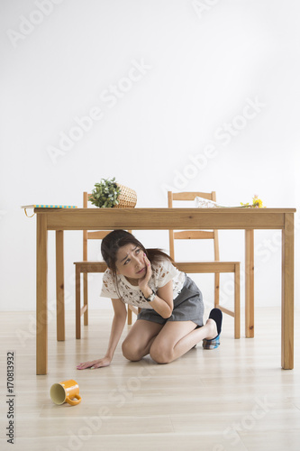地震でテーブル下に避難する女性 © milatas