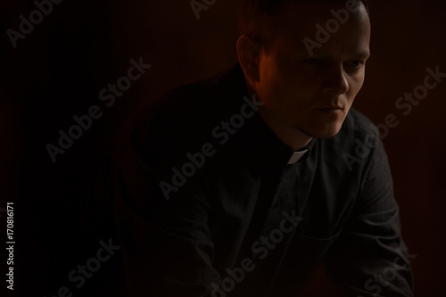 Portrait of handsome catholic priest or pastor with dog collar, dark red background.