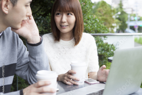 A young couple talking while watching a laptop on the cafe terrace