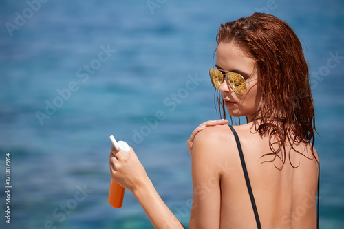Girl in bikini applying sun lotion at seaside