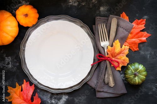 Autumn or Fall table place setting with vintage silverware decorated with autumnal leaves and decorative pumpkins with a plate on rustic wooden background for Thanksgiving Day.