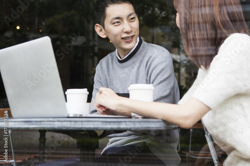A young couple talking while watching a laptop on the cafe terrace