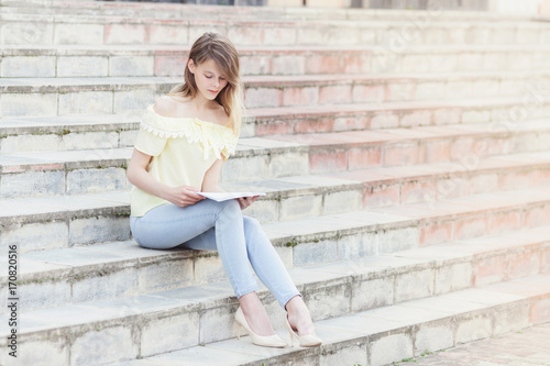 Young beautiful female student is reading on stairs © Mirrorstudio
