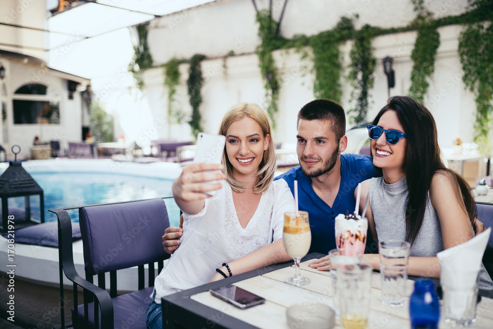 Group of young and attractive three people enjoying private party and making selfie photo. Swimming pool in background. Man with two beautiful women.