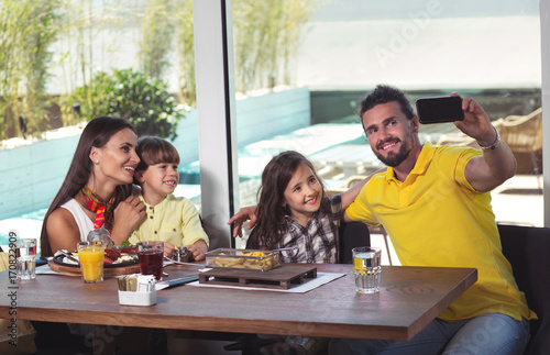 A four-member family having great time in a restaurant, make selfie photo