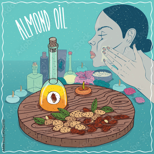 Glass Decanter of Almond oil and sweet kernels of Prunus dulcis plant. Girl applying facial mask on face. Natural vegetable oil used for skin care