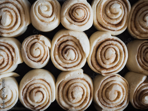 Cinnamon rolls filled with sugar, cinnamon and butter made of fresh yeast dough in black pan while rising and waiting to go in the oven