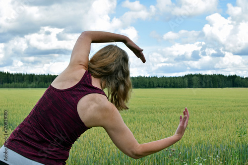 Middle aged yoga woman stretching and exercise outdoors. Rear view, field on background. photo