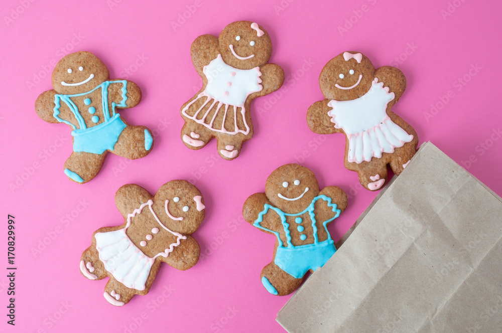 Naklejka premium Homemade gingerbread man on pink background. Boys and girls were pouring out of the package. Concept of gift. Picture for a confectionery catalog. Invitation or greeting card with copy space. Isolated