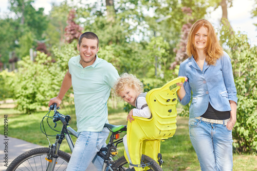Beautiful happy family cycling at the park with a child in baby bike seat safety active living people happiness riding bicycle sport concept. © serhiibobyk