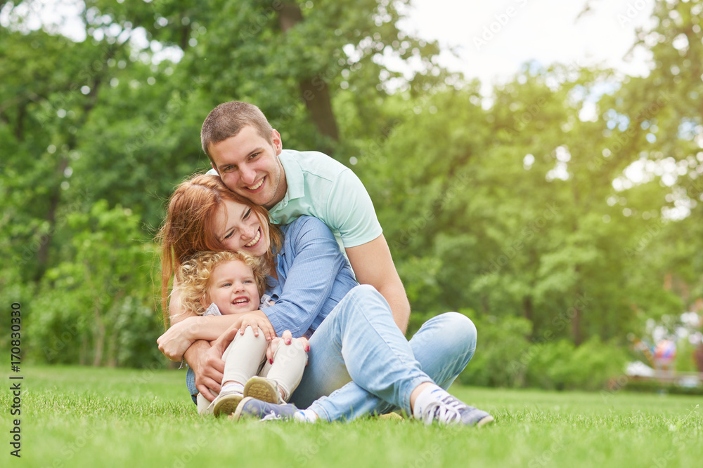 Fototapeta premium Shot of a happy young loving family having fun outdoors sitting on the grass at the park on a warm summer day hugging and cuddling copyspace parents love couples children kids daughter father mother.