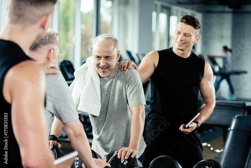 fitness trainer encouraging tired senior sportsman in gym, looking at mirror