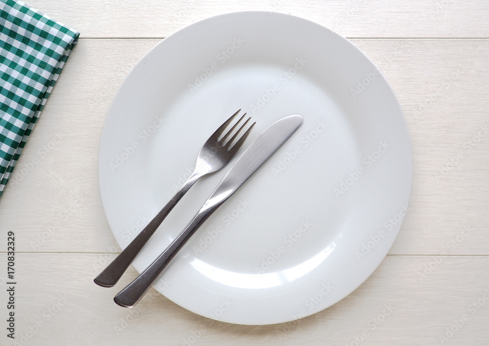 White plate and knife and fork on white wooden background White plate and knife and fork on white wooden background