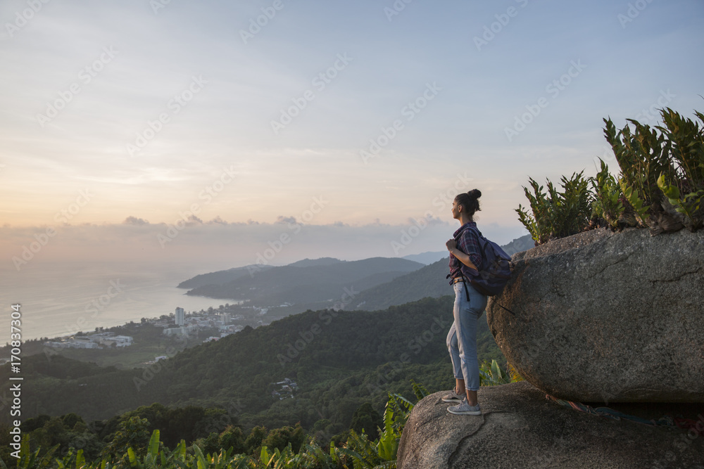 Hipster young girl with backpack enjoying sunset on peak mountain. Tourist traveler on background valley landscape view mockup.