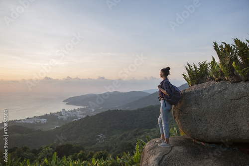 Hipster young girl with backpack enjoying sunset on peak mountain. Tourist traveler on background valley landscape view mockup.