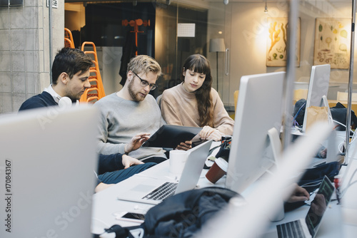 Male and female computer programmers using digital tablet at desk in office