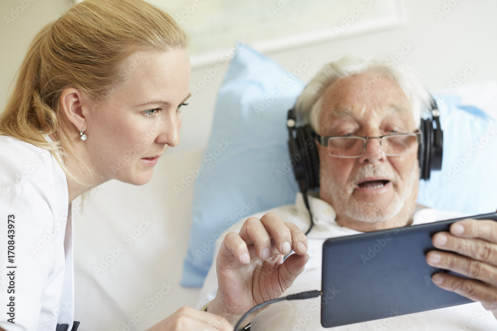 Female nurse assisting senior man in using digital tablet on hospital bed Female nurse assisting senior man in using digital tablet on hospital bed