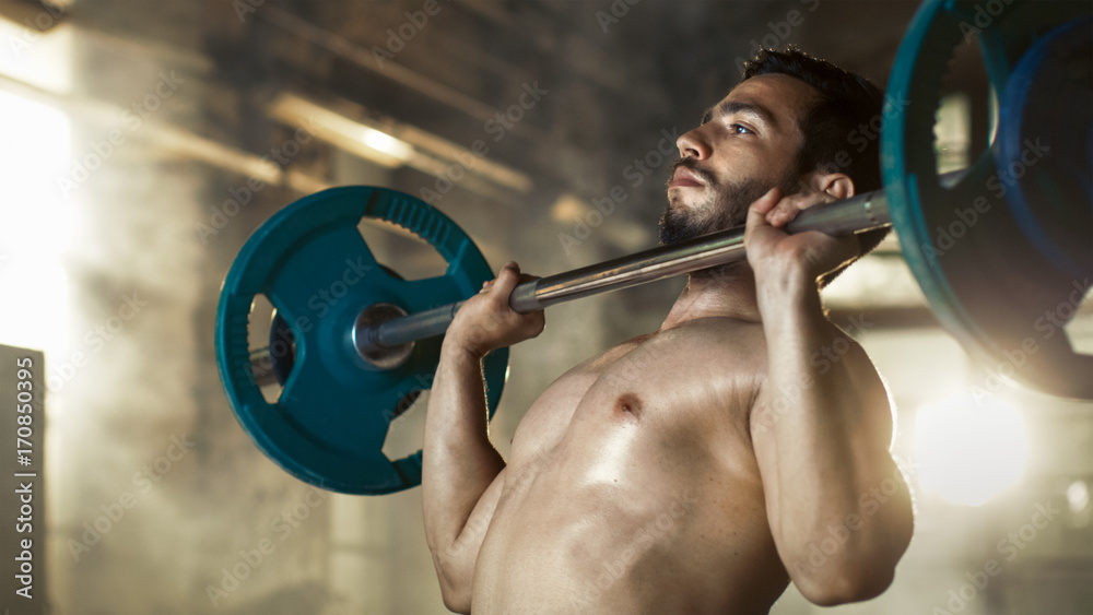Close-up of a Muscular Shirtless Man Lifting Heavy Barbell and Doing Military Press Bodybuilding Exercise in the Industrial Gym Building. Close-up of a Muscular Shirtless Man Lifting Heavy Barbell and Doing Military Press Bodybuilding Exercise in the Industrial Gym Building.